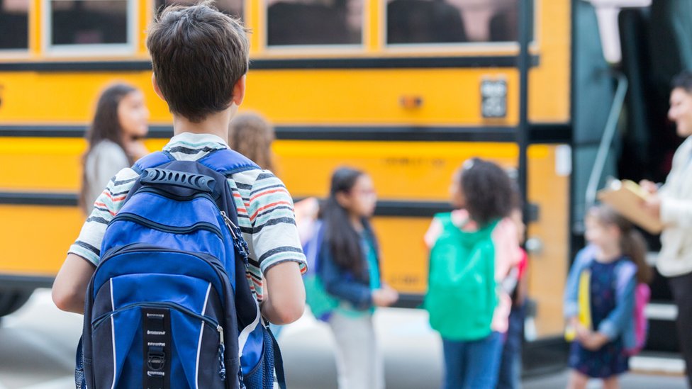 Estudiantes de espalda mirando hacia un transporte escolar.