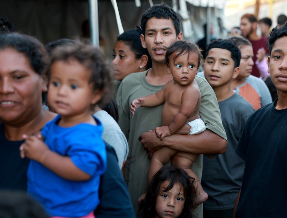 Maikel Oswaldo Mendoza sostiene a Victoria Valentina Torrelle mientras hace fila por comida tras cruzar la frontera desde México a El Paso, Texas, el 22 de septiembre de 2022.