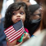 Una niña pequeña sostiene la bandera mientras USCIS da la bienvenida a nuevos ciudadanos.