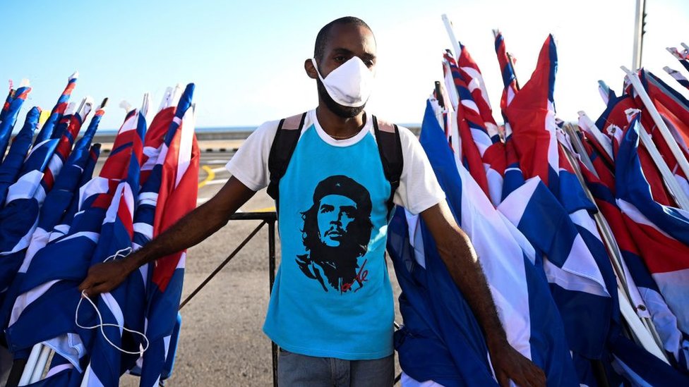 Un hombre con mascarilla entre decenas de banderas de Cuba frente al malecón de La Habana