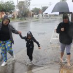 Angélica Barba, Lissette Martínez, Cassandra Williams y la pequeña Leilani cruzan una calle en medio del agua anegada.