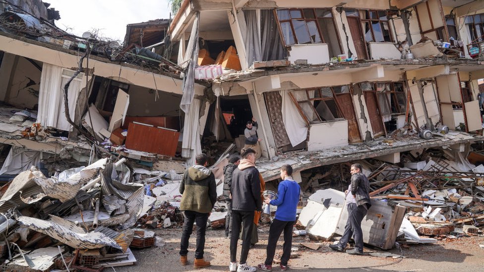 Un grupo de personas observa su edificio de apartamentos destruido.