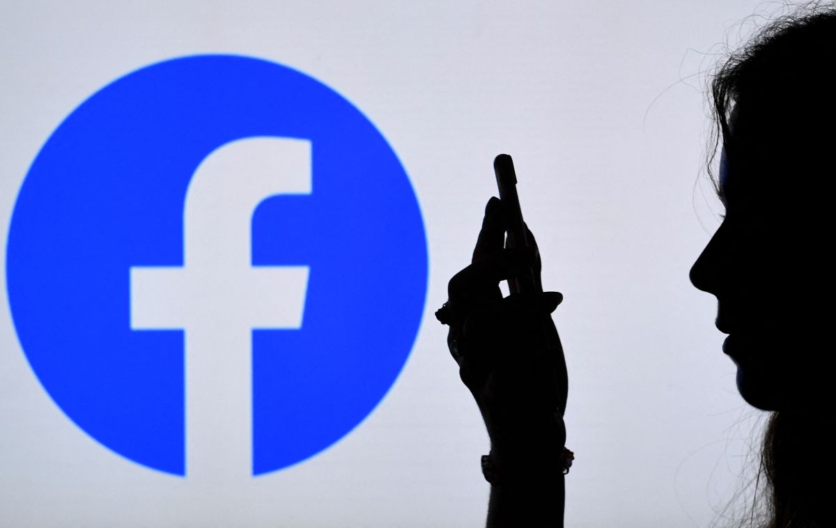 Persona mirando un teléfono con el logo de Facebook de fondo. / Foto: AFP/Getty Images