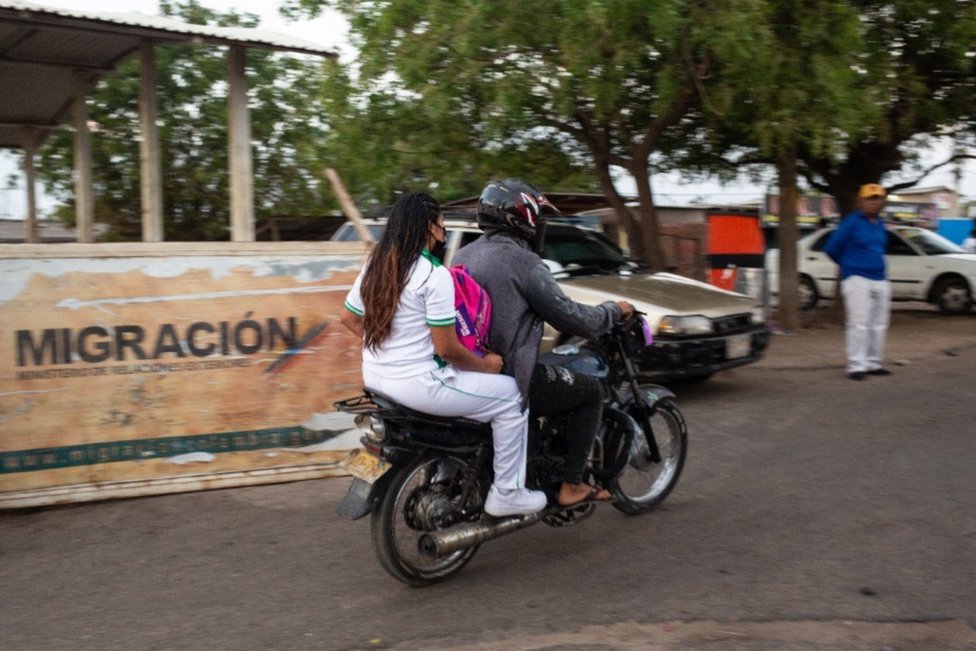 Un niño cruza la frontera en la parte trasera de una motocicleta.